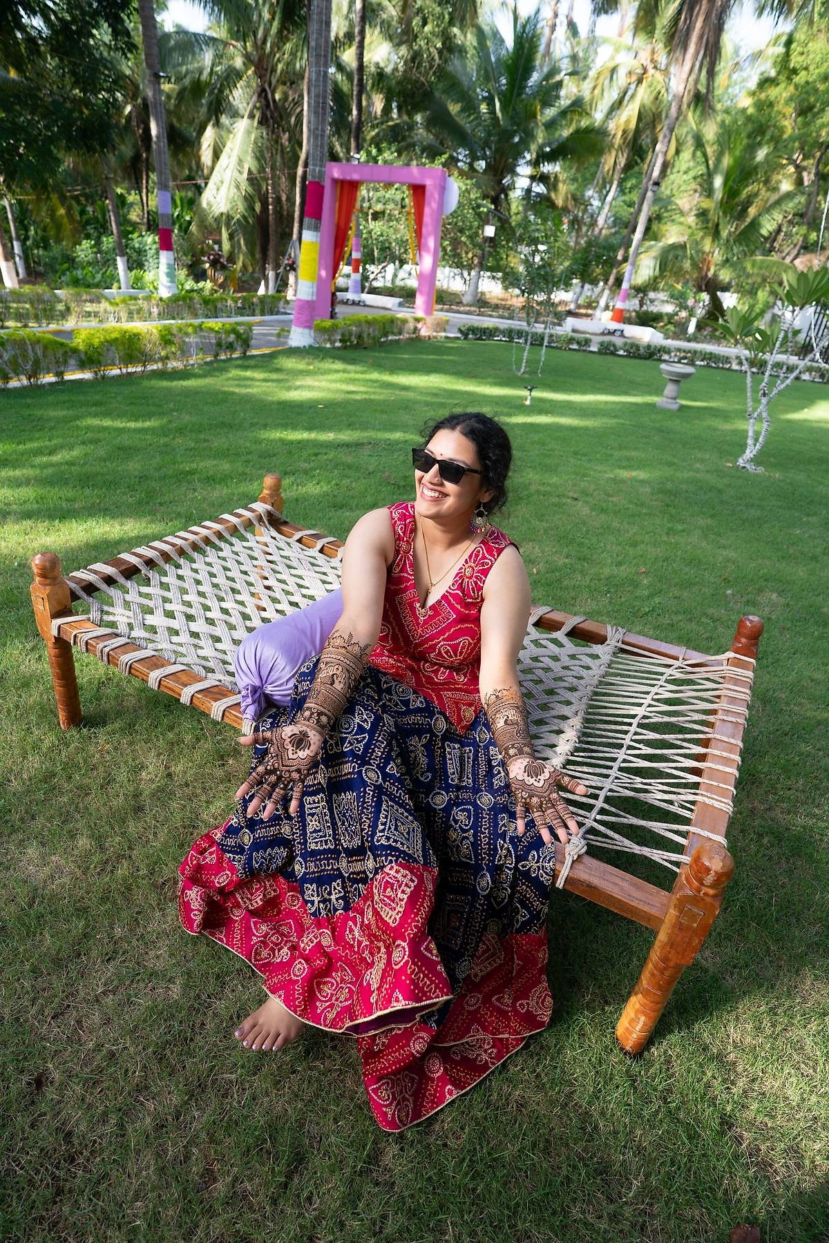 Guest with mehendi hands seated on a traditional charpai on the lawn