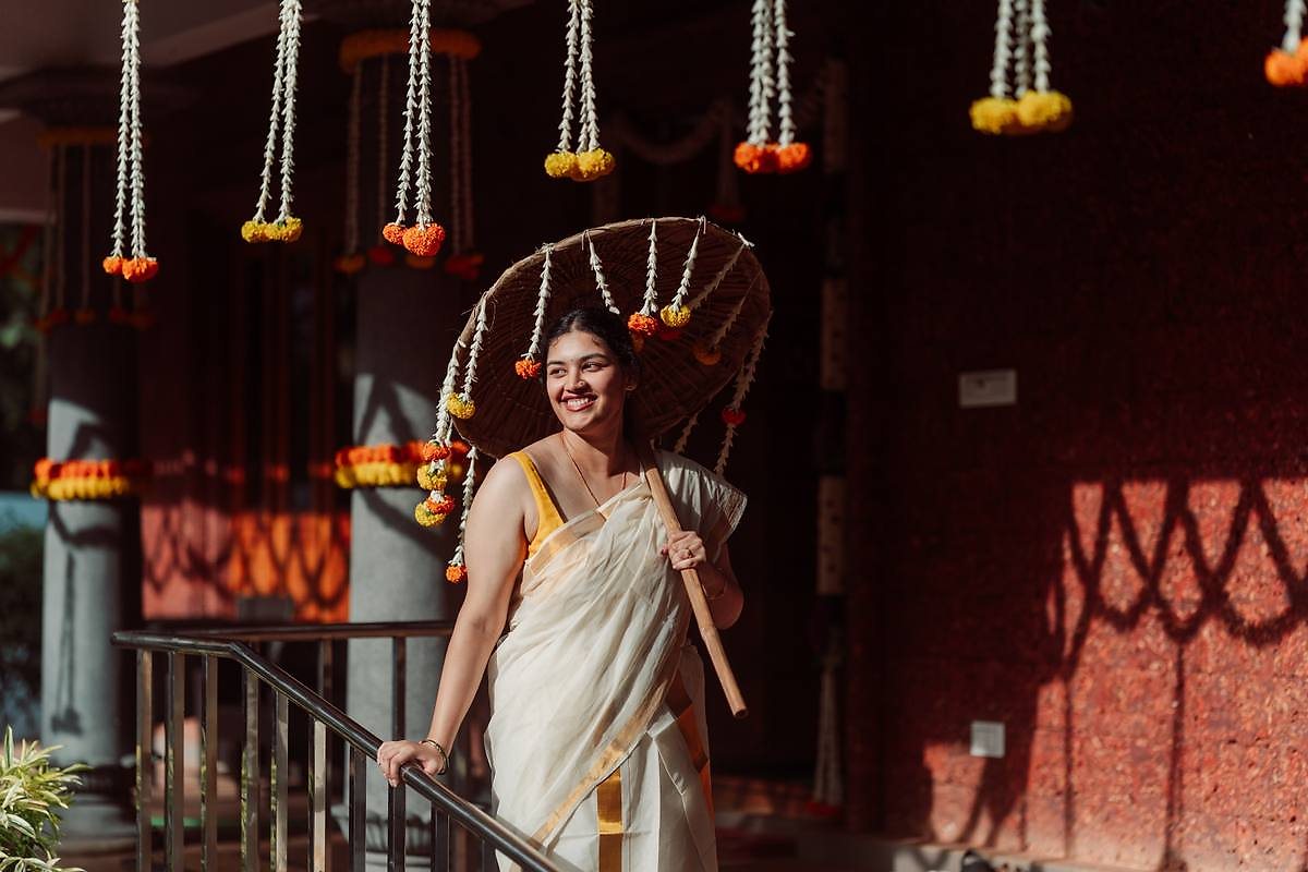 Guest in a Kerala kasavu saree under marigold garlands on the veranda